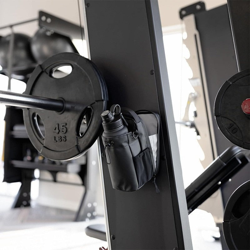 The bottle bag attached by its magnetic back to the upright of a weight machine next to a 45 lb plate