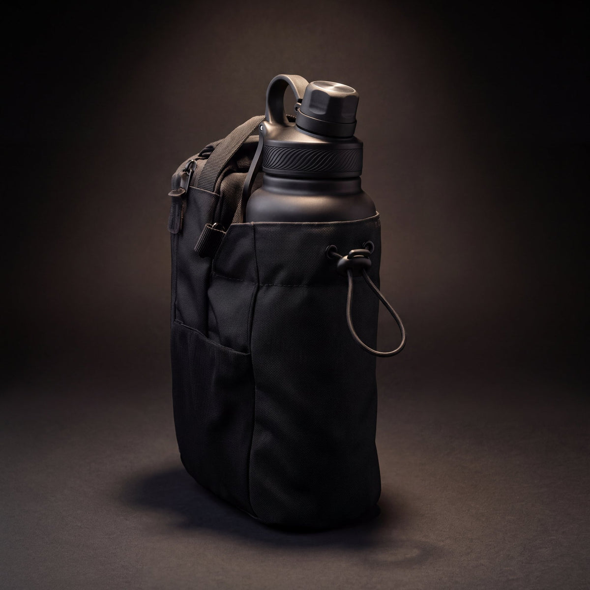 Studio photo of the black bottle bag showing the bottle sleeve, drawstring toggle, mesh pocket and carry handle